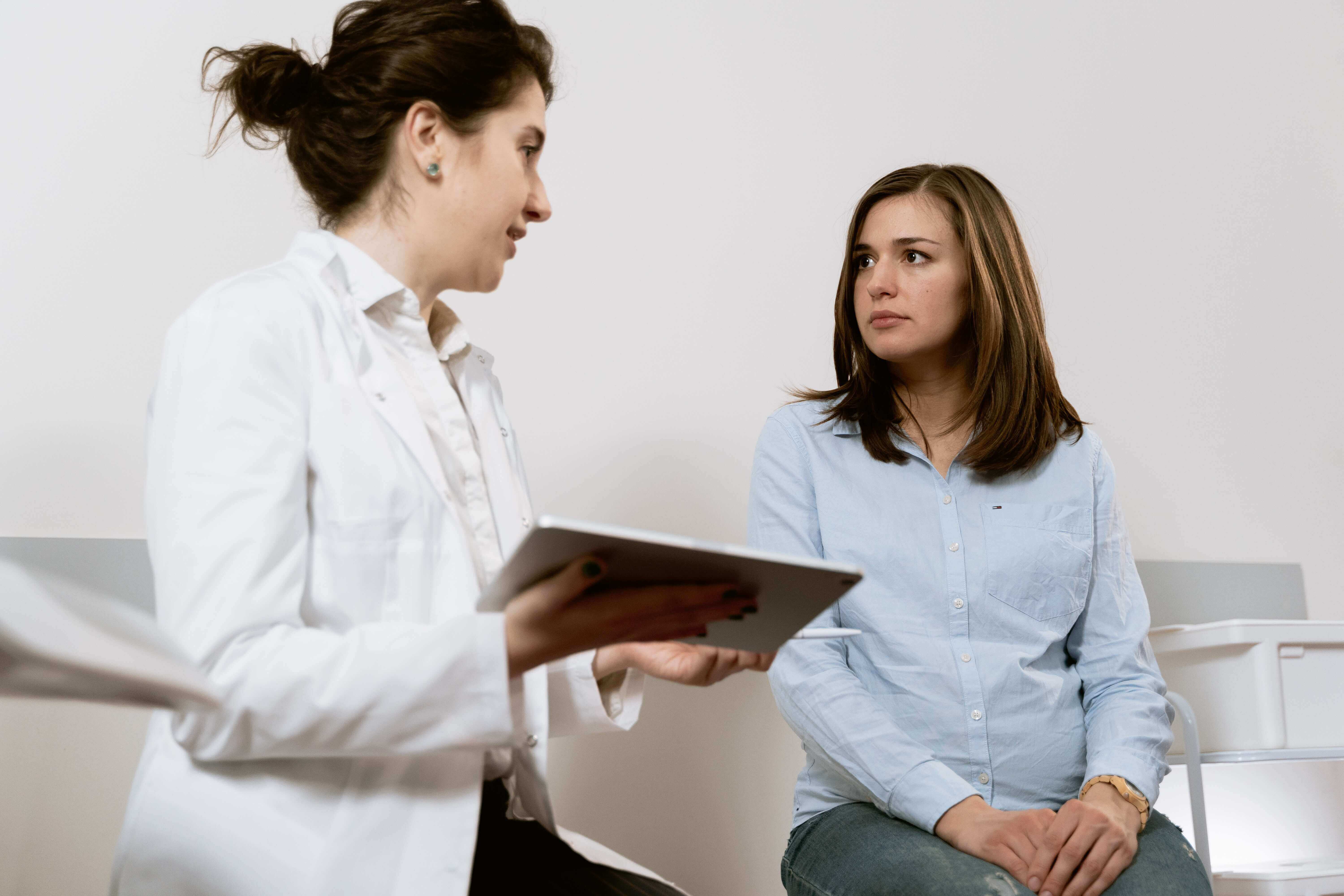 Woman sitting on a bed in an exam room and talking to her doctor